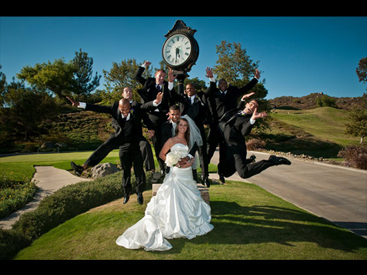 bride on course smiling with groom, as groomsmen jump in a freeze frame fashion behind them