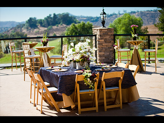 outdoor reception seating with wooden chairs, sunflower centerpieces, and navy tablecloths